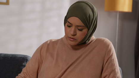 Muslimische-Frau-Mit-Hijab-Sitzt-Zu-Hause-Auf-Dem-Sofa-Und-Liest-Oder-Studiert-Den-Koran-1